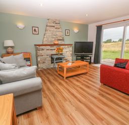 A living room with grey and red sofas a stone fireplace and a television near sliding glass doors at 64 Waterside in Lanivet