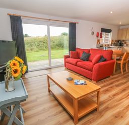 A living room with a red sofa wooden coffee table and television next to a kitchen and sliding glass doors at 64 Waterside in Lanivet