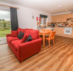 A kitchen and dining area with wooden cabinets a red sofa and sliding glass door at 64 Waterside in Lanivet