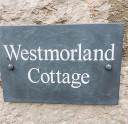 A rectangular dark plaque with white text Westmorland Cottage fixed on a stone wall