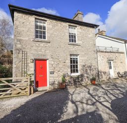 A stone cottage with a red door and wooden gate with pots outside at Westmorland Cottage in Grange-Over-Sands