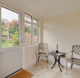 A small sunroom with two metal chairs and a table holding a bottle and book at Thorncroft in West Bay