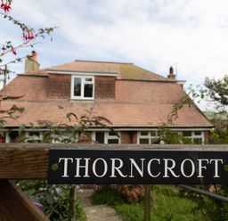 A wooden gate with a Thorncroft sign and a house with a tiled roof in the background at Thorncroft in West Bay