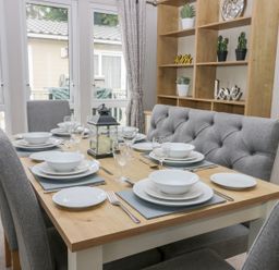 A dining room with a wooden table set for six with grey chairs and a wooden shelf with decor at Cayton Pines Cayton Bay near Scarborough