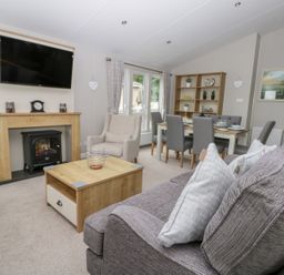 A living room with a gray sofa and cushions a wooden coffee table an armchair and a dining table with chairs at Cayton Pines in Cayton Bay near Scarborough