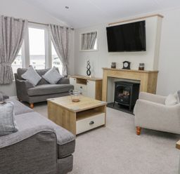 A living room with sofas a wooden coffee table a wall-mounted TV and a fireplace at Cayton Pines in Cayton Bay near Scarborough