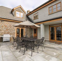 An outdoor patio with a metal dining table and chairs under a large umbrella next to a barbecue grill at Grooms Quarters at Pant y Gaseg Farm in Ammanford