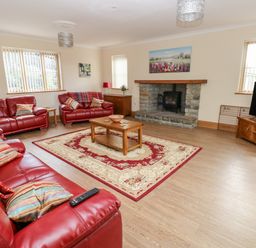 A living room with red leather sofas a wooden coffee table a rug a stone fireplace and a TV at Grooms Quarters at Pant y Gaseg Farm in Ammanford