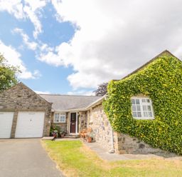 A stone house with two white garage doors and ivy covering part of the wall at Coquet View Cottage in Rothbury