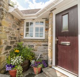 A stone cottage entrance with a dark wooden door white framed window and flower pots at Coquet View Cottage in Rothbury