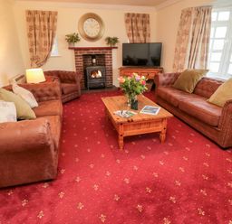 A living room with two brown sofas a brown armchair a wooden coffee table with flowers a fireplace and a television at Coquet View Cottage Rothbury