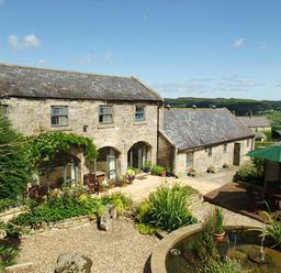 A stone building with arched windows a patio garden and a round pond with a fountain at The Steadings in Rothbury