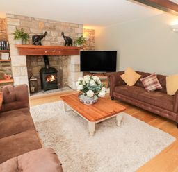 A living room with brown sofas a wooden coffee table with flowers a stone fireplace and a television at The Steadings in Rothbury