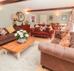 A living room with multiple sofas a wooden coffee table with flowers and a dining table in the background at The Steadings in Rothbury