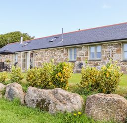 A stone cottage with several windows and a patio table with chairs and umbrella in a garden at Pen Tewan in Sennen