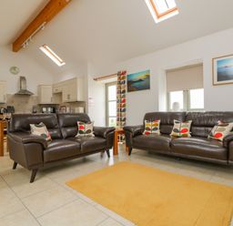 A living room with two brown leather sofas with patterned cushions a yellow rug and a kitchen area at Pen Tewan in Sennen