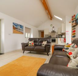 A living room with two brown leather sofas and patterned cushions an orange rug and a kitchen area at Pen Tewan in Sennen