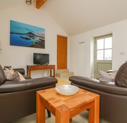 A sitting area with two brown leather sofas a wooden table with a bowl a wooden door a small TV on a wooden stand a floor lamp and landscape pictures at Pen Tewan in Sennen