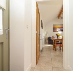 A hallway leading to a dining area with a wooden table and chairs a black leather sofa a floor lamp and wall art at An Gwel in Sennen