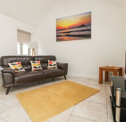 A living room with a brown leather sofa and patterned cushions a yellow rug and a television at An Gwel in Sennen