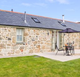 An outdoor patio area with a table and chairs under an umbrella next to a stone house with a lawn at An Garth in Sennen