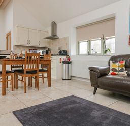 A kitchen and dining area with a wooden table and chairs and a leather sofa at An Garth in Sennen