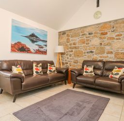A sitting room with two brown leather sofas cushions on a rug and a stone feature wall at An Garth in Sennen