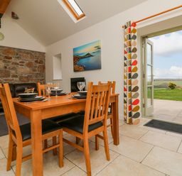 A dining area with a wooden table set for four near an open door leading to a patio with a green lawn at An Garth in Sennen