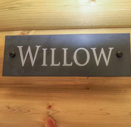 A wooden wall with a metal sign reading Willow at Willow Lodge in St Florence