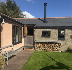 An outdoor view of a cabin with a wood pile and garden at The Hideout in Llangrove