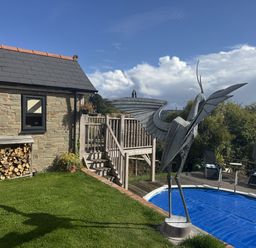 A house with a wooden deck, metal sculpture, and a pool at The Hideout in Llangrove