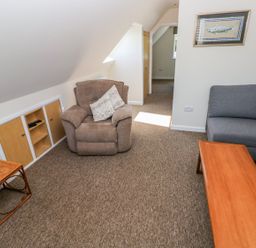 A living room with a brown armchair a grey sofa a wooden coffee table and a small wooden side table at Mill View in Neyland