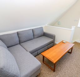 A grey sectional sofa and a wooden coffee table in a room with carpeted floor and a window at Mill View in Neyland