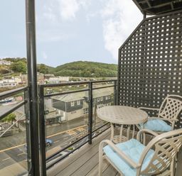A balcony with two chairs and a round table overlooking a street and river at Harbour View Apartment in Looe