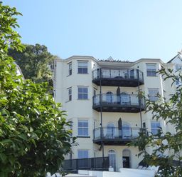 A multi-story residential building with balconies surrounded by green trees at Harbour View Apartment in Looe