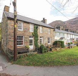 A row of stone and painted terraced houses with small front gardens and a grassy area in front at Brackenbury Cottage in Beddgelert