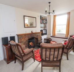 A living room with a fireplace two armchairs TV and a window with yellow curtains at Brackenbury Cottage in Beddgelert