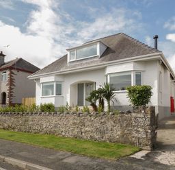A white detached house with a stone wall and driveway at Y Gogarth in Benllech
