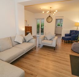 A living room with beige sofas a blue armchair a wood stove and wooden flooring at Y Gogarth in Benllech