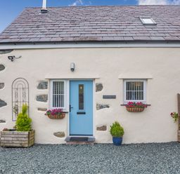 A stone house exterior with a blue door two windows flower pots and gravel ground at Marchlyn in Deiniolen
