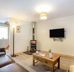 A living room with a wood stove a wall-mounted TV a wooden coffee table two leather sofas and a floor lamp at Marchlyn in Deiniolen