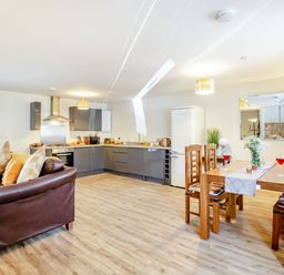 An open plan kitchen and dining area with a brown leather sofa a wooden dining table with chairs and a kitchen with grey cabinets at Marchlyn in Deiniolen