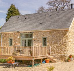 A stone house with a wooden deck and potted plants outside at The Apple Barn at Wyke Farm in Lyme Regis