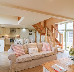 An open plan living room with beige sofa and wooden coffee table beside stairs at The Apple Barn at Wyke Farm in Lyme Regis