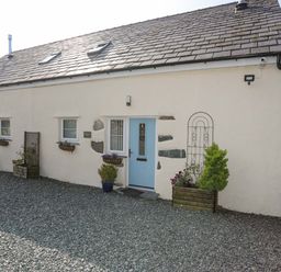A cottage with blue doors small windows flower pots and gravel in front at Ffynnon Bach in Deiniolen