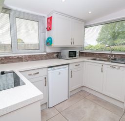 A kitchen with white cabinets a microwave a small refrigerator a stovetop and two windows with blinds at 201 Norton Park in Dartmouth
