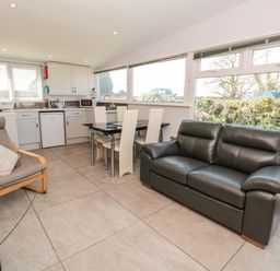 An open kitchen and dining area with a black leather sofa and beige chairs at 201 Norton Park in Dartmouth