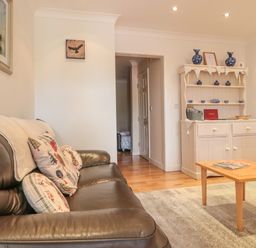 A living room with a leather sofa pillows and a wooden coffee table in front of a white cabinet with blue ceramics at Church Road Annexe in Cinderford