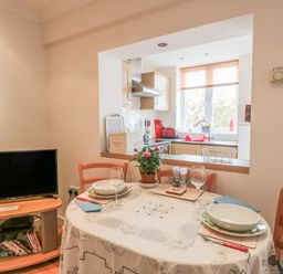 A dining area with a round table set for two near a kitchen with wooden cabinets and appliances at Church Road Annexe in Cinderford