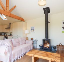 A living room with a pink striped sofa a wooden coffee table and a wood stove at The Shippon at Wyke Farm Lyme Regis